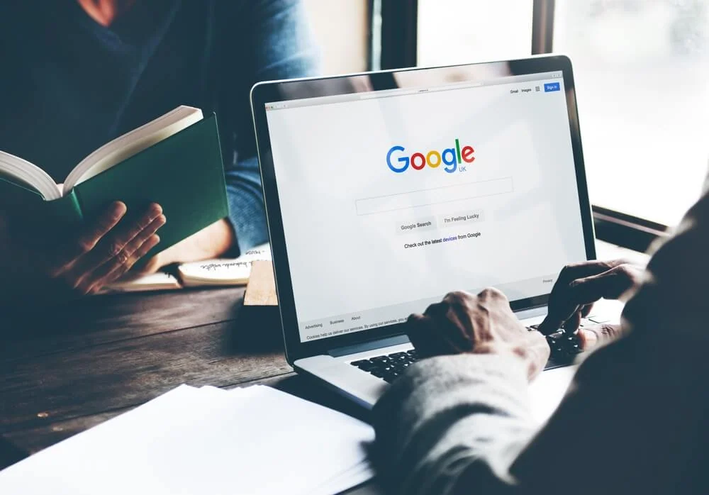 A marketer researches SEO services on a laptop as a colleague studies content marketing.