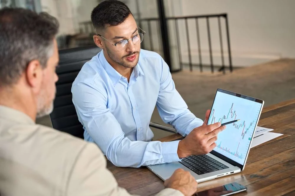 Two men at a digital marketing agency review SEO data on a laptop for strategy planning.