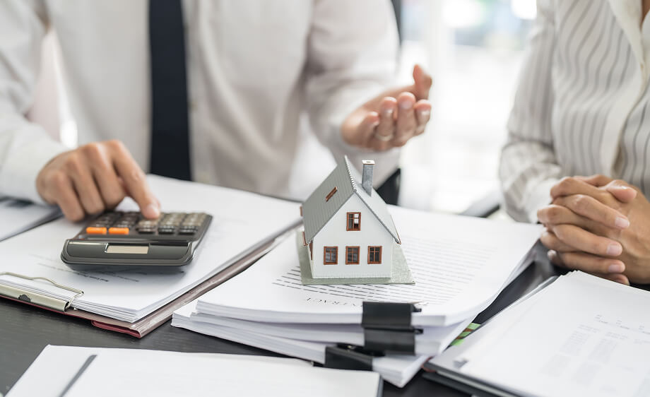 Two people discuss digital marketing agency services with documents and a model house.