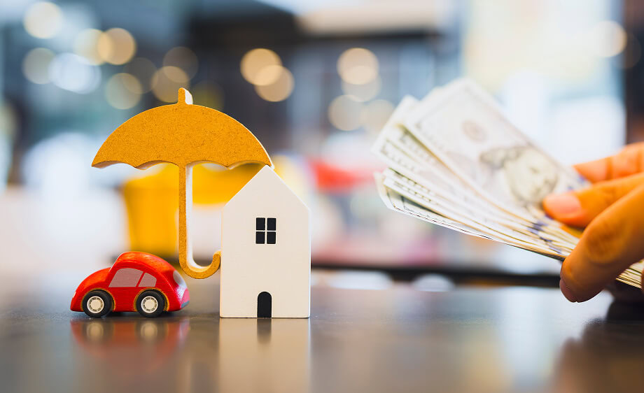 A hand with cash near a toy car and house under umbrella, symbolizing a digital marketing agency’s web development and SEO services for financial protection.