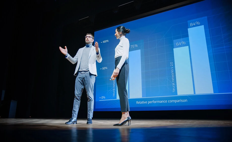 Two presenters on stage share digital marketing agency insights with SEO and social media data on a bar graph.