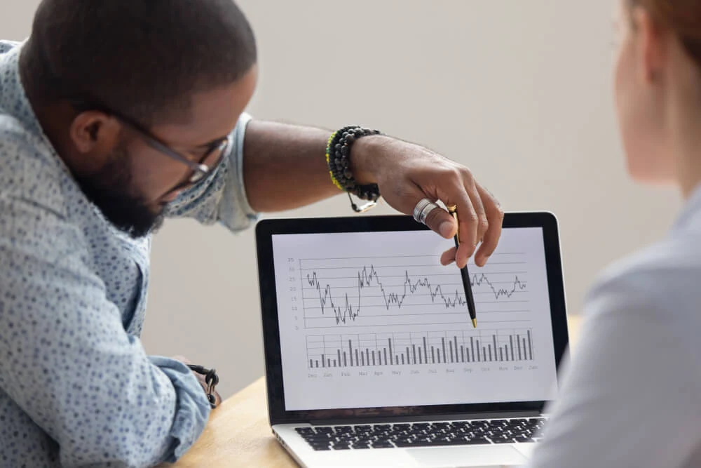 Two marketers analyze SEO and paid media results on a laptop performance chart.