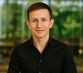 A smiling man in a black shirt stands in a digital marketing agency office.