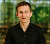 A smiling man in a black shirt stands in a digital marketing agency office.