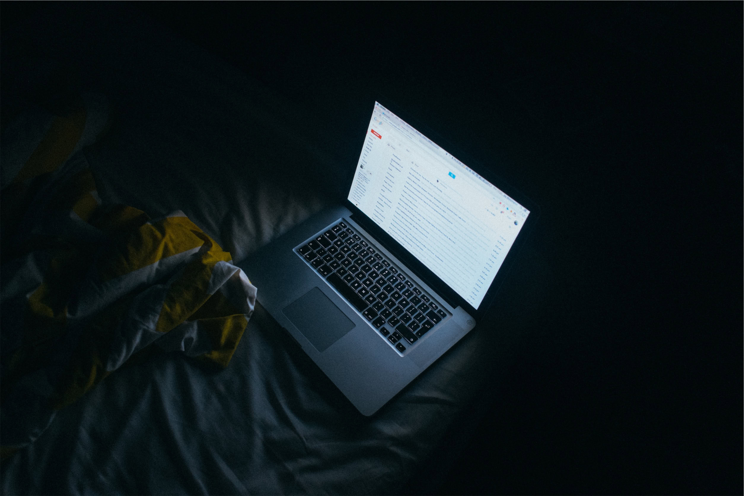 A laptop showing a digital marketing agency email inbox sits on a bed in low light.