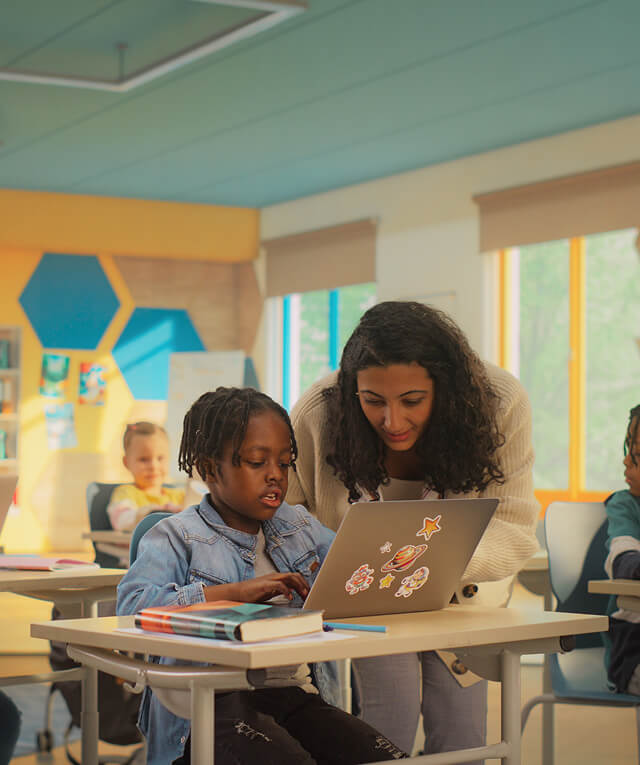 A teacher helps a student on a laptop, highlighting SEO and content marketing in education.