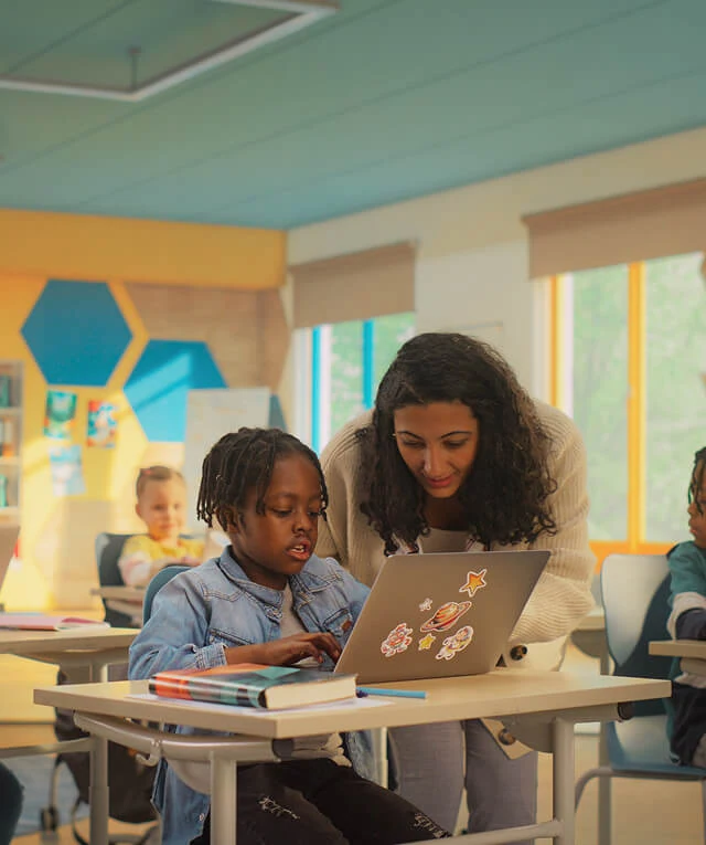 A teacher helps a student on a laptop, highlighting SEO and content marketing in education.