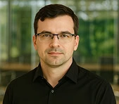 A digital marketing agency professional in glasses stands indoors with blurred windows.