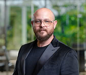 A bearded digital marketing agency expert stands indoors with greenery behind him.