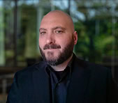 A bearded man in a black suit at a digital marketing agency office background.