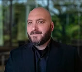 A bearded man in a black suit at a digital marketing agency office background.