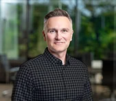 A man at a digital marketing agency stands indoors with windows and greenery behind.