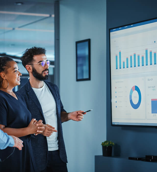 Three people in an office review SEO services and analytics on a large digital marketing agency presentation screen.