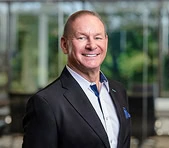 A digital marketing agency professional smiles indoors with greenery in the background.