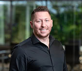 A digital marketing agency expert with a beard stands indoors near a bright window.