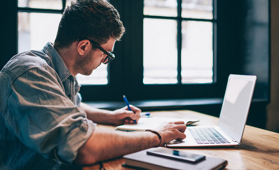 A man at a wooden table writes SEO and content marketing notes for a digital agency.