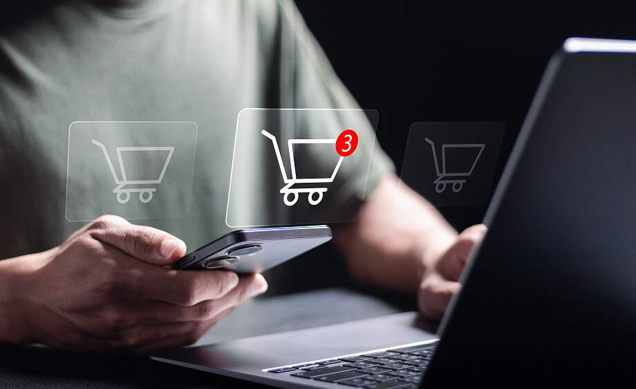 A user holds a phone by a laptop with a shopping cart, showing digital marketing agency web development and ecommerce solutions.