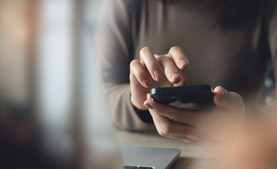 A marketer uses a smartphone for SEO and social media tasks beside a laptop.