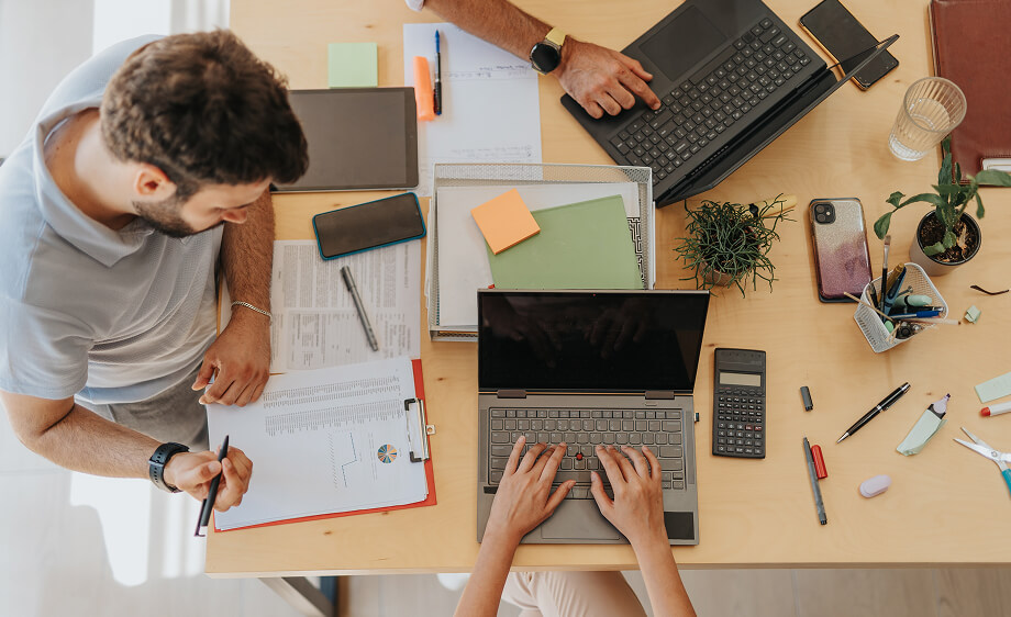 Two digital marketing agency team members work on laptops with SEO and social media notes.