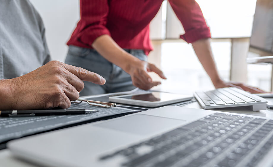 Two marketers collaborate at a desk with devices, planning SEO and web content strategy.