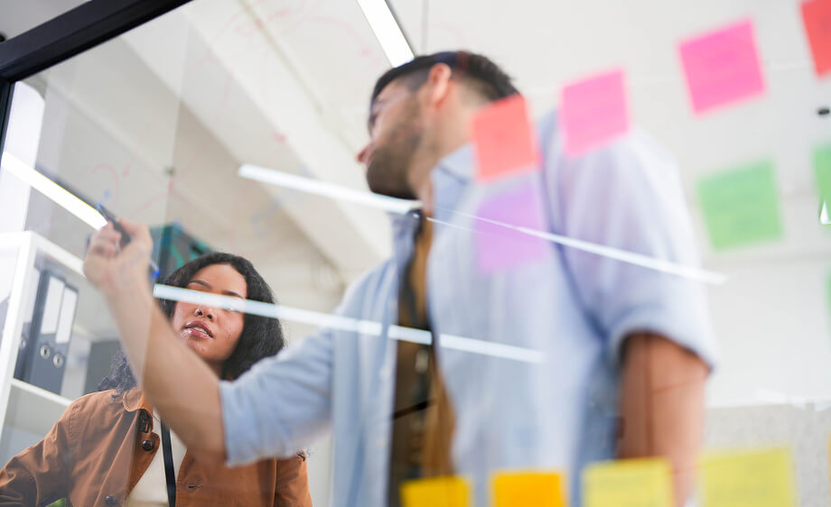 Two marketers brainstorm video content at a digital marketing agency glass wall.