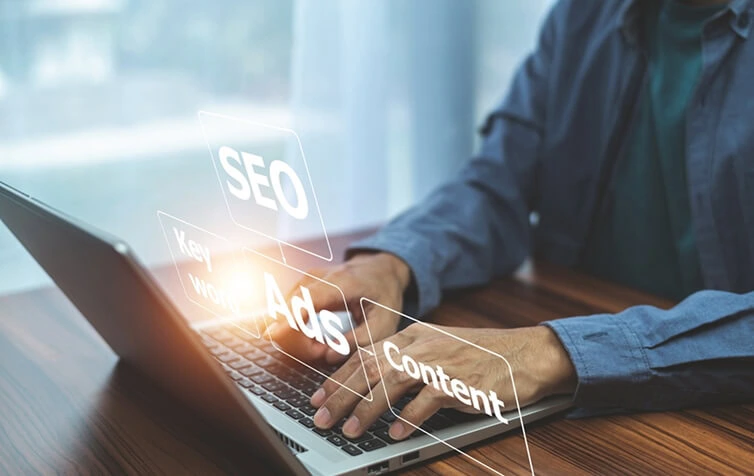 Marketer at laptop with virtual SEO, content marketing, and paid media agency terms.