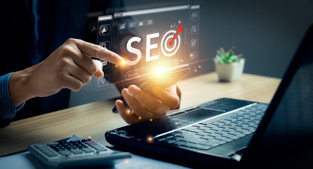 A digital marketing agency expert uses a smartphone for SEO services and content marketing at a desk with a laptop.