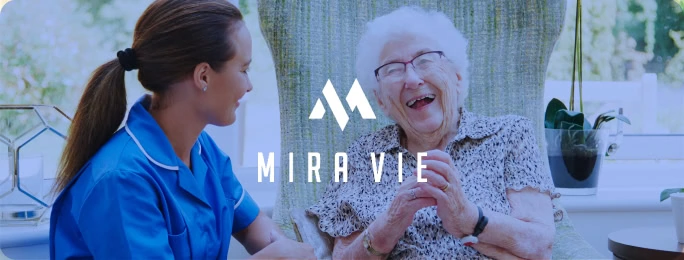 A nurse and senior laugh in a bright room, with "Mira Vie" logo, ideal for content marketing and social media agency websites.