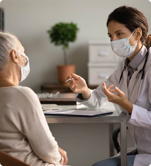 A masked healthcare provider consults with an older patient at a desk, promoting telehealth SEO services.