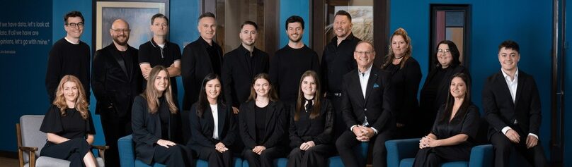 Sixteen digital marketing agency team members in formal attire pose in a modern office.