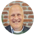 Smiling bald man in a suit, representing a digital marketing agency, by a brick wall.