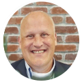 Smiling bald man in a suit, representing a digital marketing agency, by a brick wall.