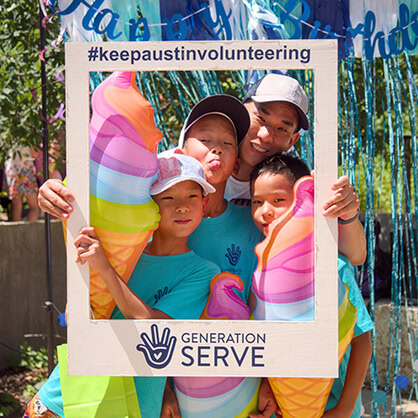 Four people from a digital marketing agency pose at a community event, holding a “#keepaustinvolunteering” frame.