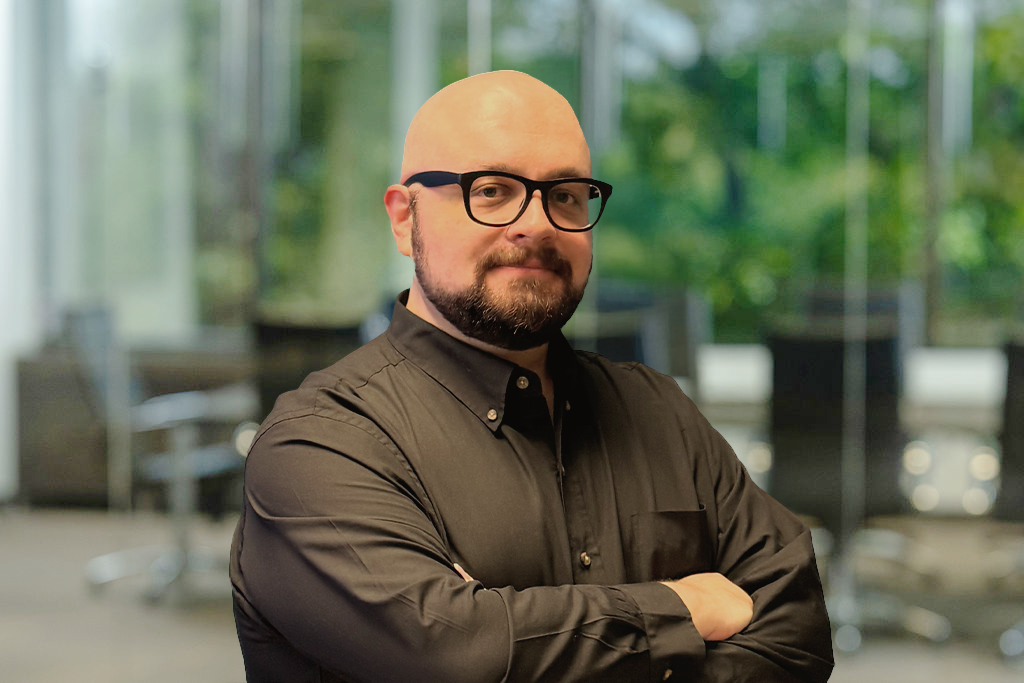 A man with glasses and a beard, arms crossed, in a digital marketing agency office.