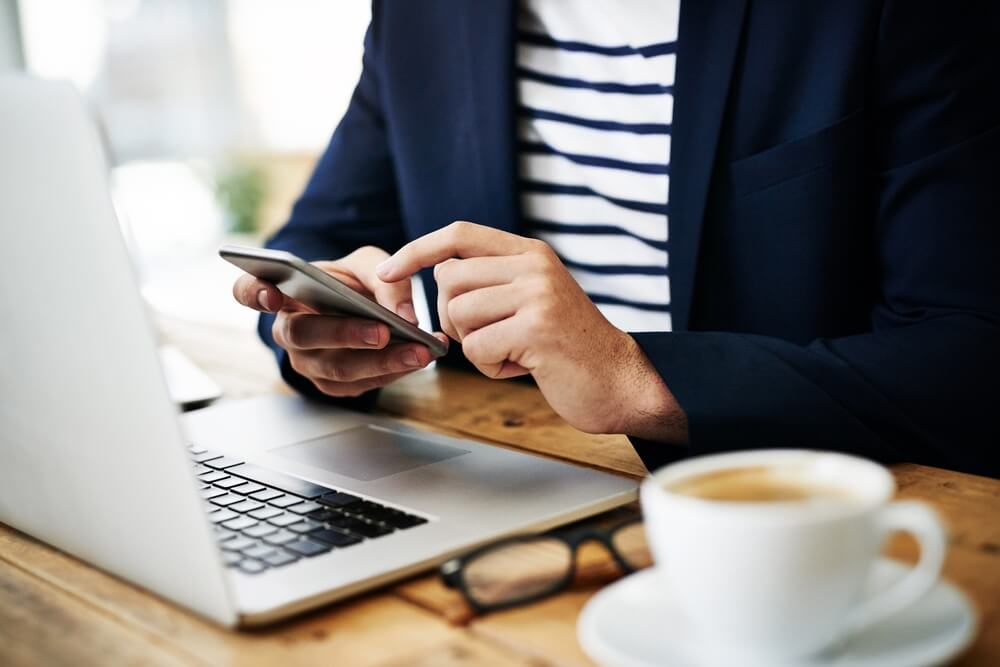 Digital marketing agency expert in blazer uses smartphone at table with laptop, planning SEO services and social media marketing strategies.