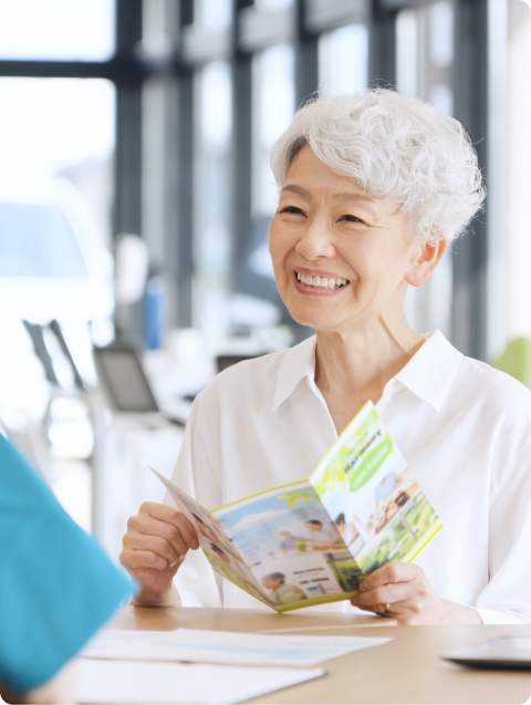 An older woman with short white hair smiles holding a Senior Living brochure at a digital marketing agency desk.